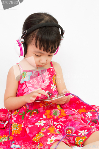 Image of Chinese little girl on headphones holding mobile phone