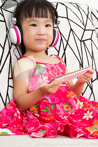 Image of Chinese little girl on headphones holding mobile phone