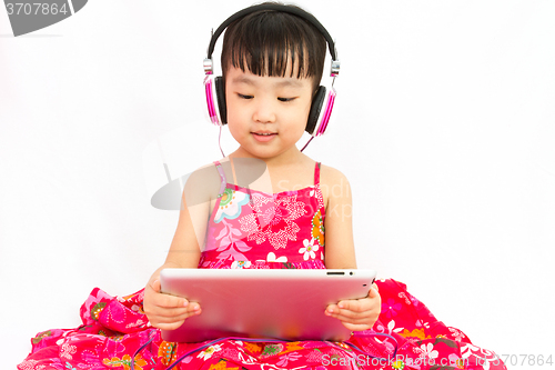 Image of Chinese little girl on headphones holding tablet