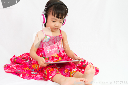 Image of Chinese little girl on headphones holding tablet