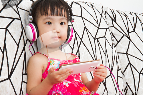 Image of Chinese little girl on headphones holding mobile phone
