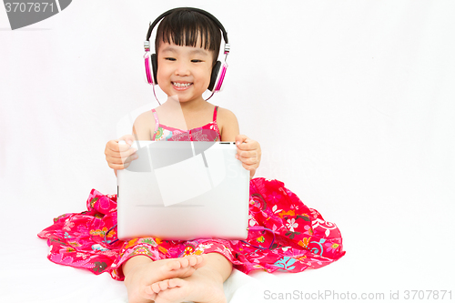 Image of Chinese little girl on headphones holding tablet