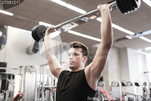 Image of young man flexing muscles with barbell in gym