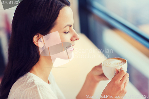 Image of smiling young woman drinking coffee at cafe