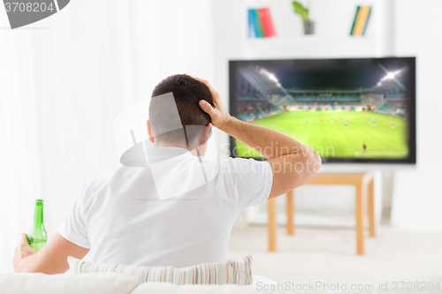 Image of man watching football and drinking beer at home