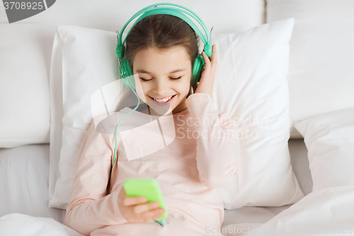 Image of happy girl lying in bed with smartphone at home