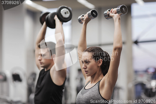 Image of smiling man and woman with dumbbells in gym