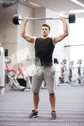 Image of young man flexing muscles with barbell in gym