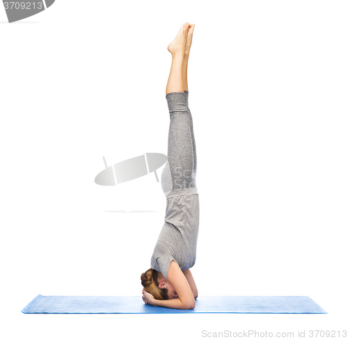 Image of woman making yoga in headstand pose on mat