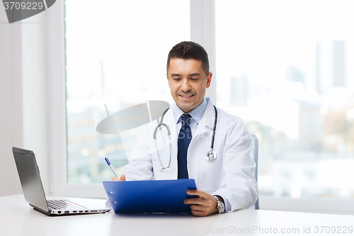 Image of happy doctor with clipboard and laptop in office