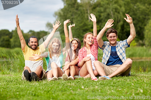 Image of group of smiling friends waving hands outdoors