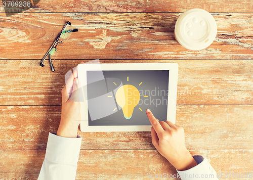 Image of close up of hands with lighting bulb on tablet pc