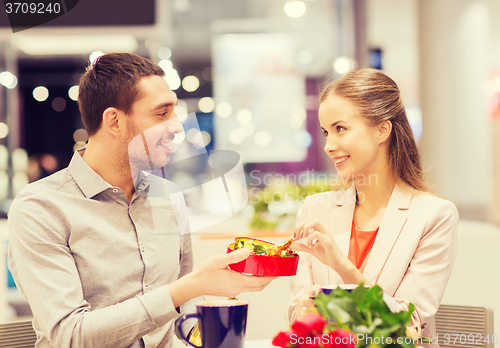 Image of happy couple with present and flowers in mall