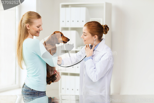 Image of happy woman with dog and doctor at vet clinic