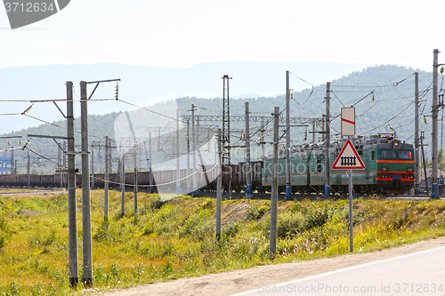 Image of Big green electric locomotive with cars going by rail