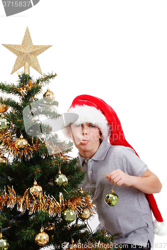 Image of Boy with santa hat sticking out tongue at  the Christmas tree