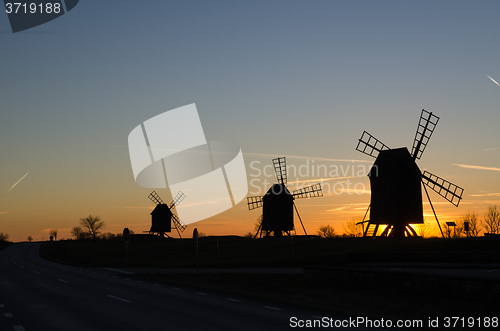 Image of Windmills silhouettes by roadside at sunset