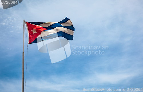 Image of Cuban flag flying in the wind on a backdrop of blue sky.