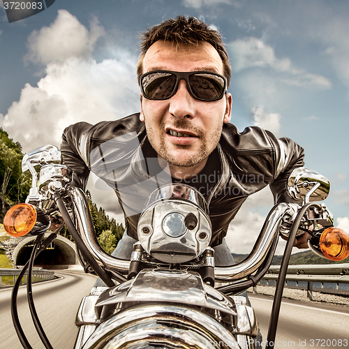 Image of Funny Biker in sunglasses and leather jacket racing on mountain 