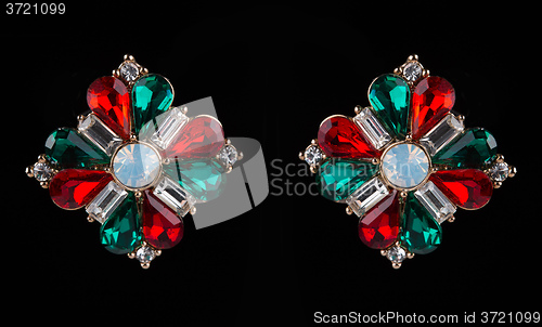 Image of earring with colorful red and green gems on black background