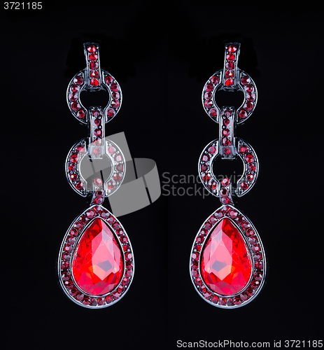 Image of earring with colorful red gems on black background