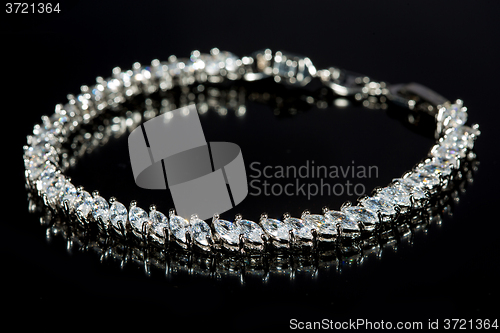 Image of silver bracelet with diamonds on black background. 