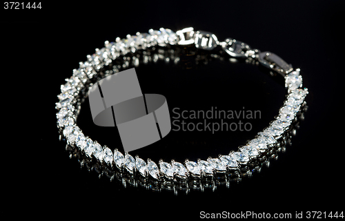 Image of silver bracelet with diamonds on black background. 