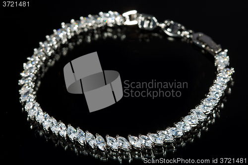 Image of silver bracelet with diamonds on black background. 
