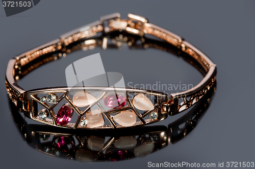 Image of golden bracelet with precious stones on grey background