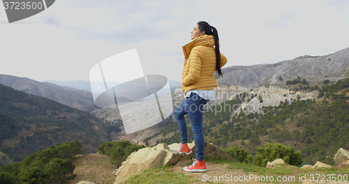 Image of Woman in yellow coat near mountain valley