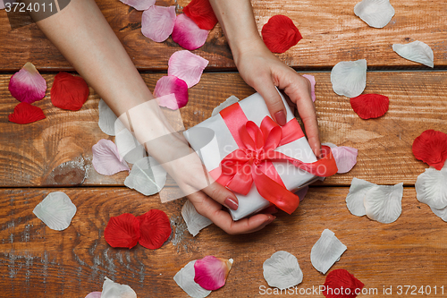 Image of Valentines Day gift and Female hands on wooden background with petals