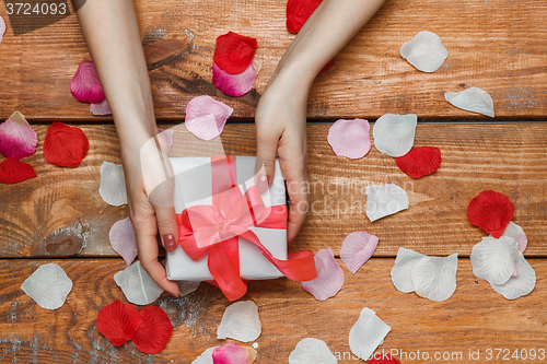 Image of Valentines Day gift and Female hands on wooden background with petals