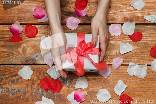 Image of Valentines Day gift and Female hands on wooden background with petals