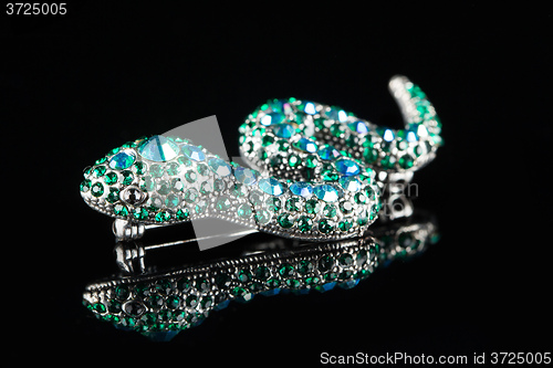 Image of brooch in the form of a snake. green stones. black background