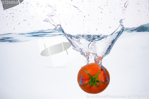 Image of red tomato dropped into blue water on white