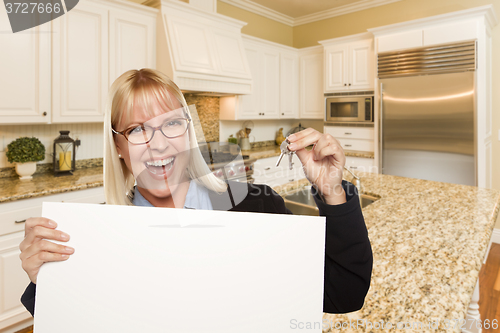 Image of Young Woman Holding Blank Sign and Keys Inside Kitchen
