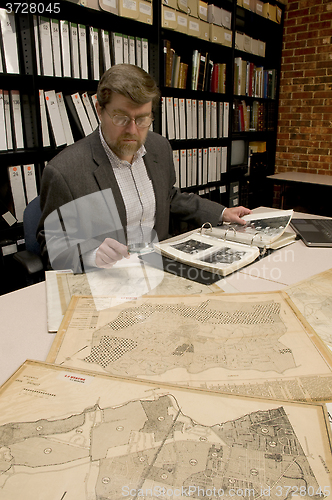 Image of Researcher in archive, searching through maps and photographs.