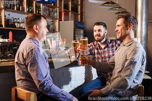 Image of Happy friends drinking beer at counter in pub