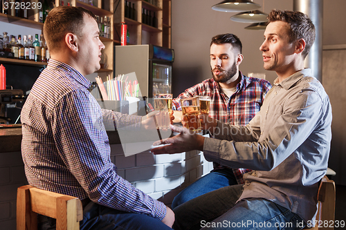 Image of Happy friends drinking beer at counter in pub