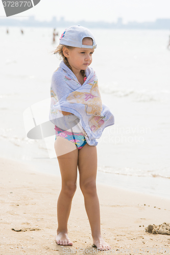 Image of Frozen girl standing on the beach wrapped in a towel