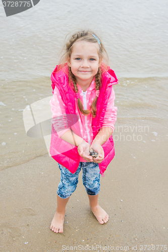 Image of Three year old girl standing on the beach with shells in hand