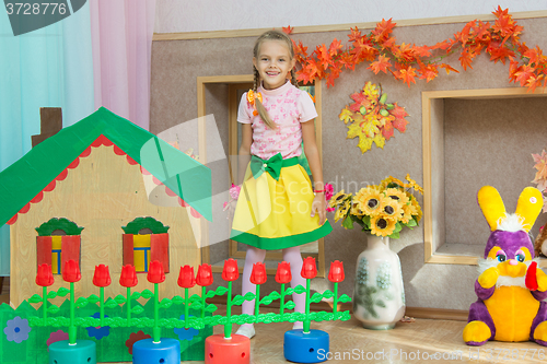 Image of Six year old girl stands in the scenery of a country house on the matinee in kindergarten