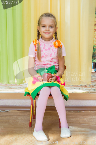 Image of Girl sitting on a chair with an apple in his hand on a matinee in kindergarten