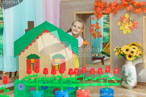 Image of The girl looks out from behind the scenery a country house in the matinee in kindergarten