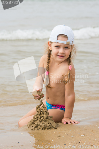 Image of  The three-year girl builds a sand castle on the beach