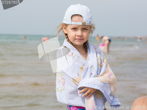 Image of Three year old girl standing on the beach wrapped in a towel