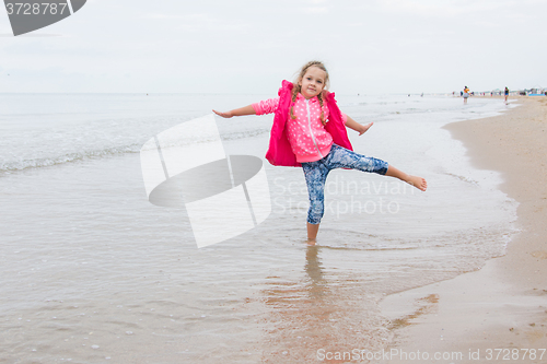 Image of Three year old girl having fun stood on one leg on the beach