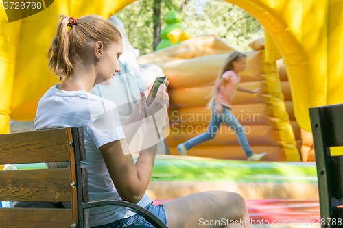 Image of Young mother with a child at the phone waiting inflatable trampolines