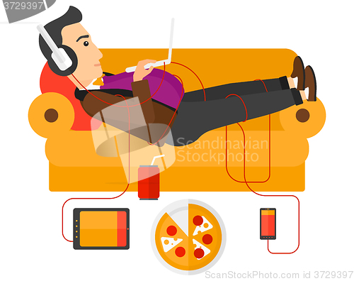 Image of Man with gadgets lying on sofa.