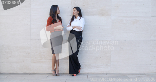 Image of Two young women leaning on a wall chatting